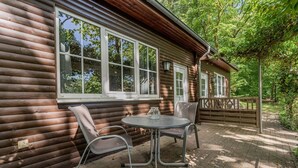 A log cabin with a patio area featuring a table and chairs, large windows, and a wooden deck. - Binzer Waldhof - Igelhaus (Binz)