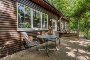A log cabin with a patio area featuring a table and chairs, large windows, and a wooden deck. - Binzer Waldhof - Igelhaus (Binz)
