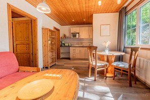 A cozy room with a wooden ceiling, a dining table with chairs, a kitchen area, and a large window.