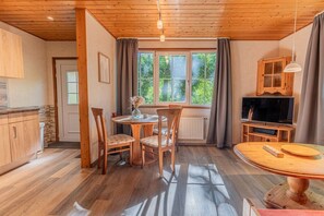 A cozy room with a wooden ceiling, a dining table with chairs, a TV, and a window with curtains.