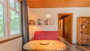 A room with a wooden table, red sofa, and a wooden cabinet. - Binzer Waldhof - Igelhaus (Binz)