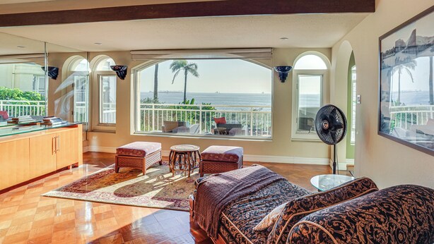 Ampla sala de estar com grande janela vista para o oceano, um ventilador e mesa de bilhar.