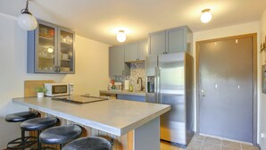 A kitchen with a central island, bar stools, stainless steel appliances, and a cabinet with glass doors. - Walk to Chair Lift: Mtn-View Schweitzer Studio! (Sandpoint)