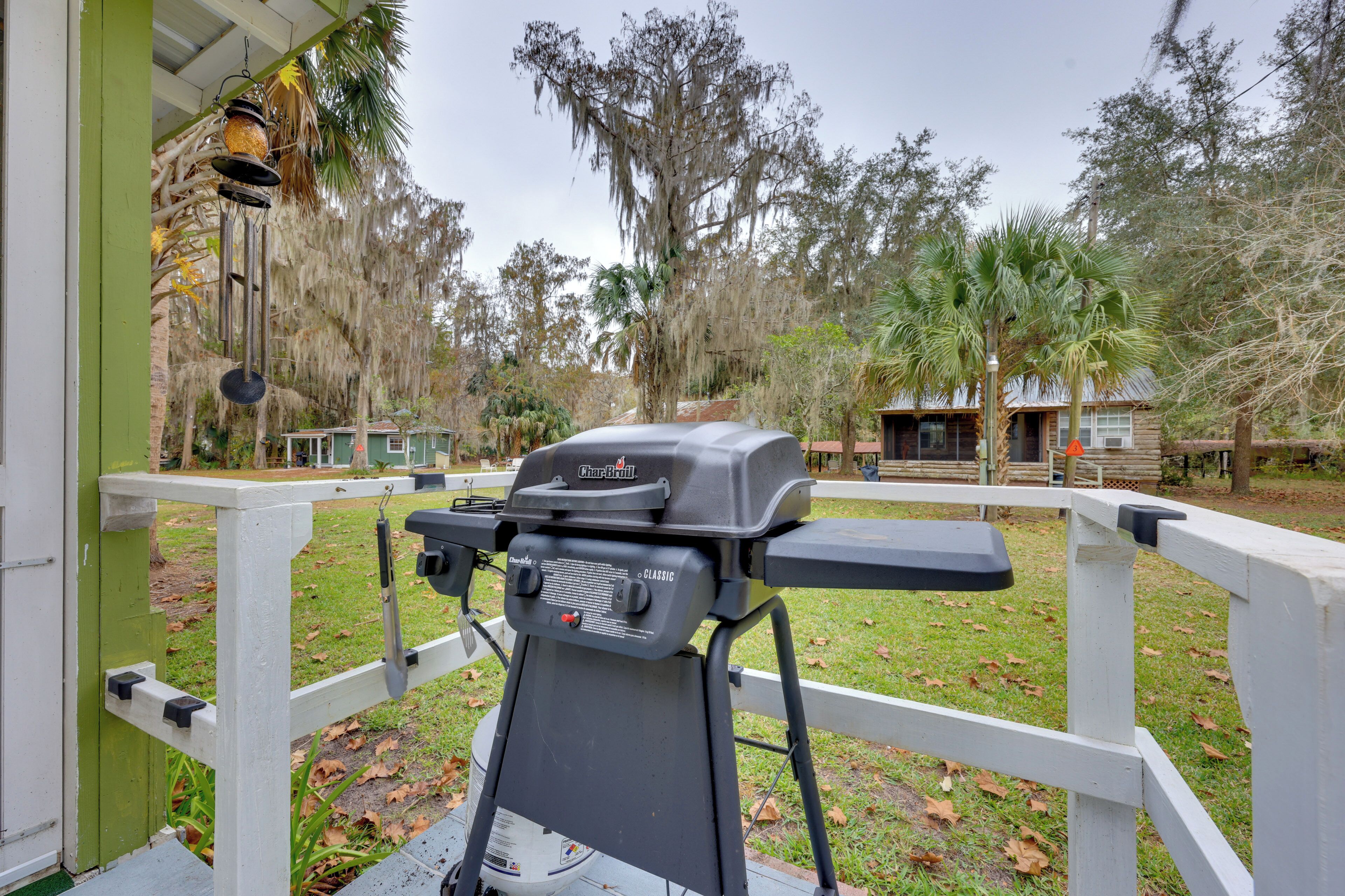 A barbecue grill on a white deck with a view of a house and trees.