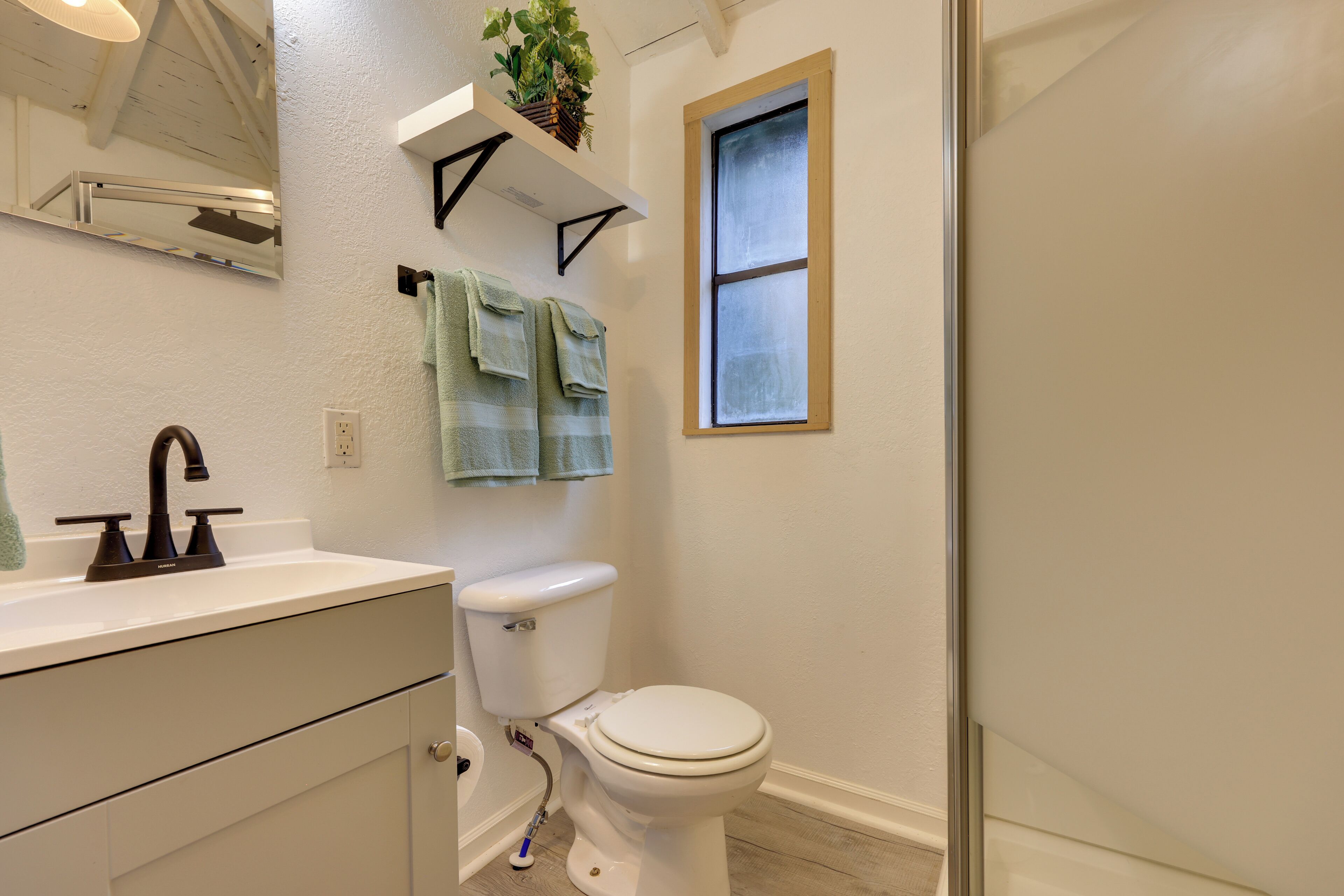 A bathroom with a white sink, black faucet, white toilet, and a window with a wooden frame.