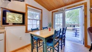 A dining area with a wooden table and chairs, a television mounted on the wall, and a large window with blinds. - Fish, Boat & Explore: Cross Creek Cabin w/ Dock! (Hawthorne)