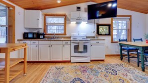 A kitchen with white cabinets, a microwave, stove, and a TV mounted on the wall. - Fish, Boat & Explore: Cross Creek Cabin w/ Dock! (Hawthorne)