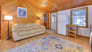 A cozy room with wooden walls and ceiling, a beige sofa, a patterned rug, a wooden side table, and a refrigerator. - Fish, Boat & Explore: Cross Creek Cabin w/ Dock! (Hawthorne)