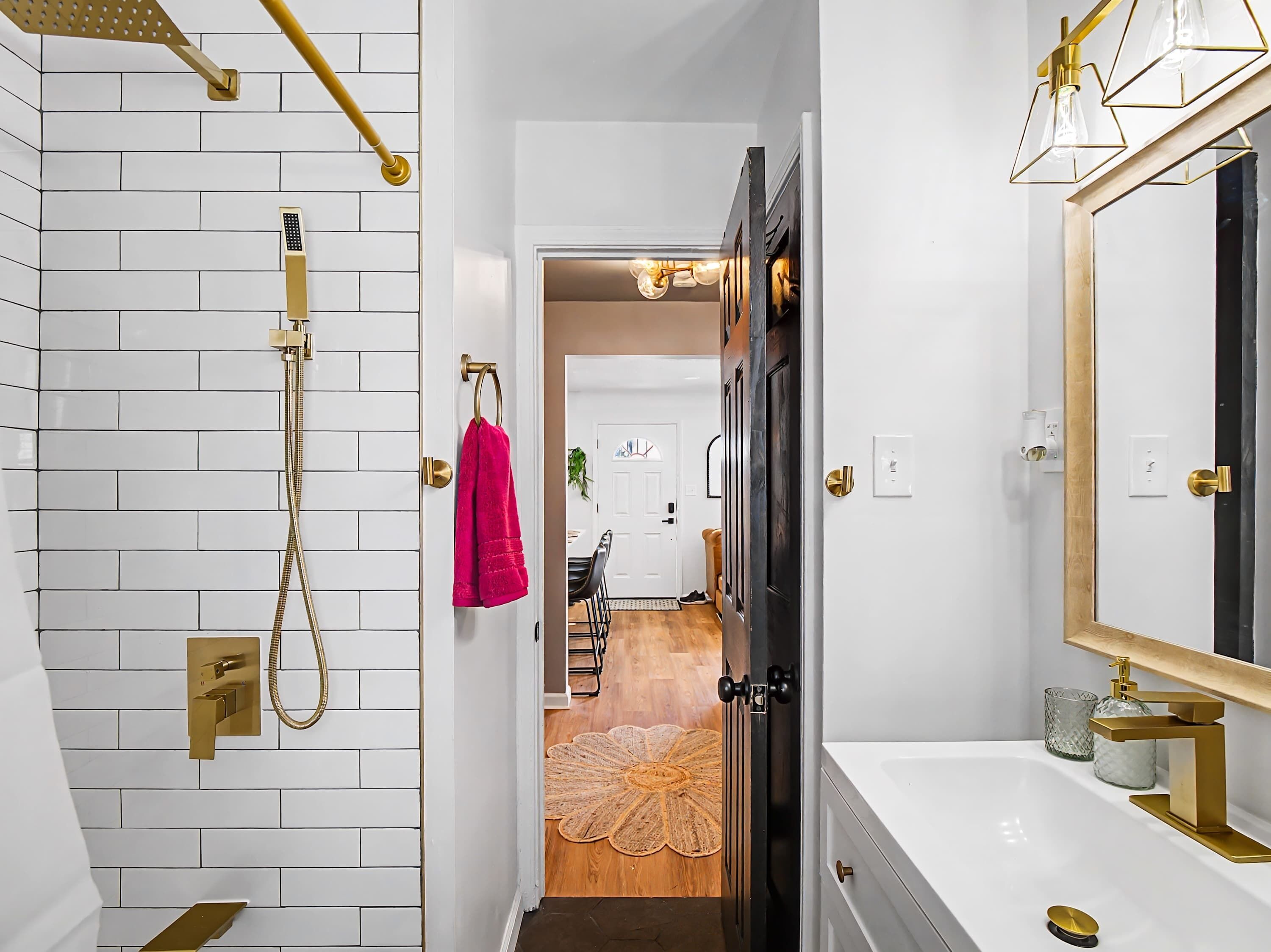 A modern bathroom with a white tiled shower area, a golden showerhead, and a large mirror with a gold frame.