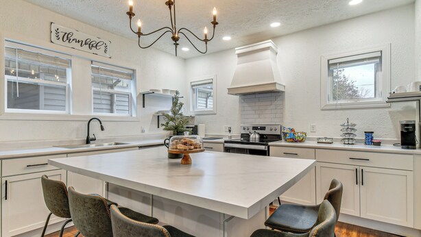 A modern kitchen with a central island, bar stools, and a chandelier. - Walk to Marshall University: Home w/ Private Yard! (Huntington)
