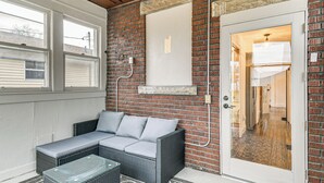 A room with a brick wall, a glass door, a wicker sofa, and a patterned rug. - Walk to Marshall University: Home w/ Private Yard! (Huntington)