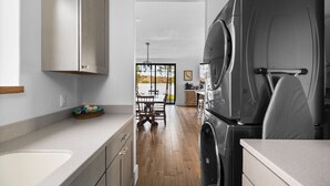 A modern kitchen with a large refrigerator, a washing machine, and a dining area with wooden chairs and a table. - [Modern Lake House] hot tub, dock, sandy shoreline, kayaks, foosball, Bellaire. (Bellaire)