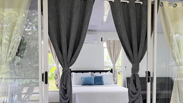 A bedroom with a bed, curtains, and a view through a glass door. - Toucan House (Valle Azul)