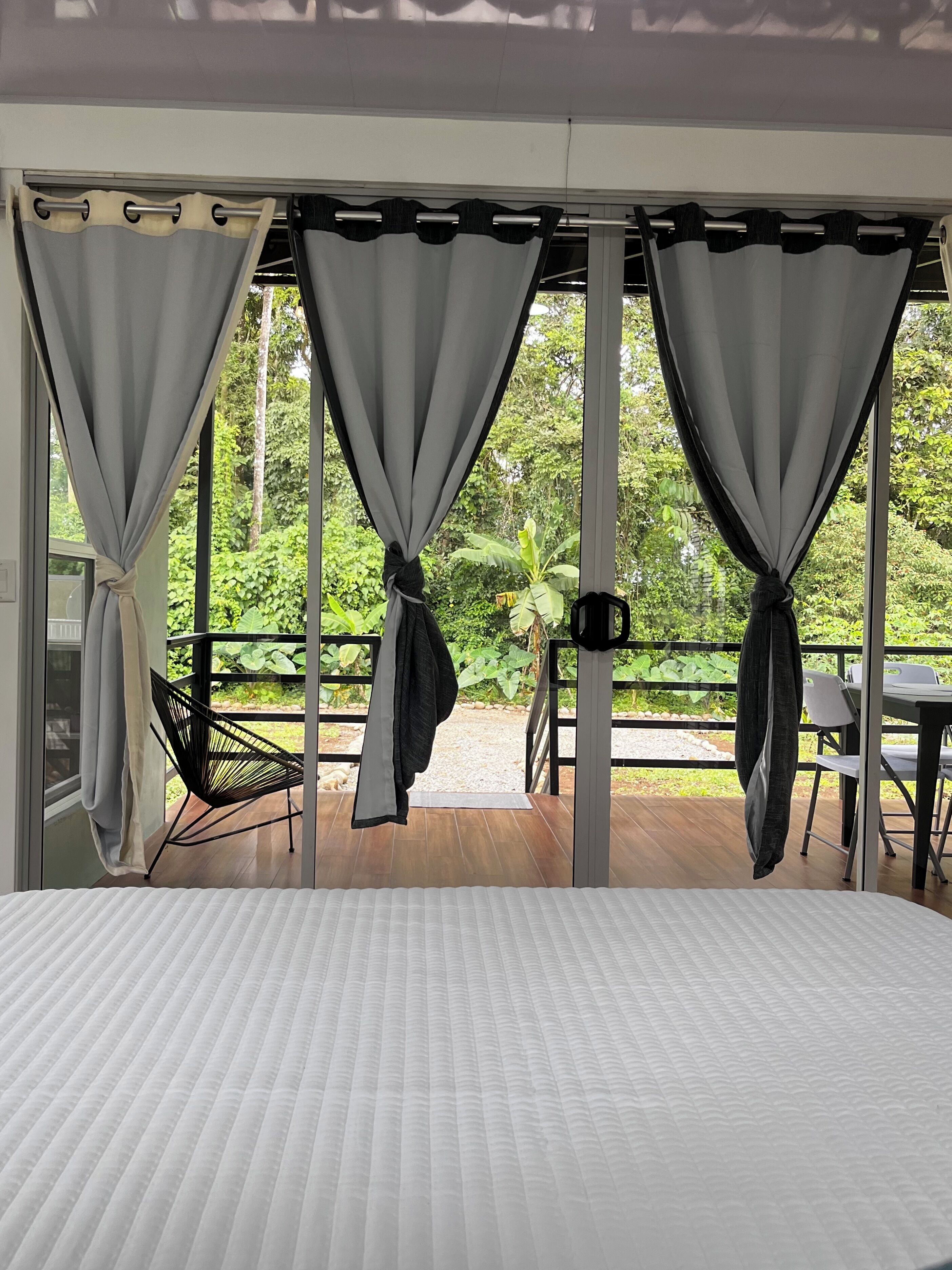 Una habitación con cama, cortinas recogidas y vistas a un jardín.