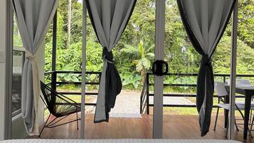Una habitación con cama, cortinas recogidas y vistas a un jardín.