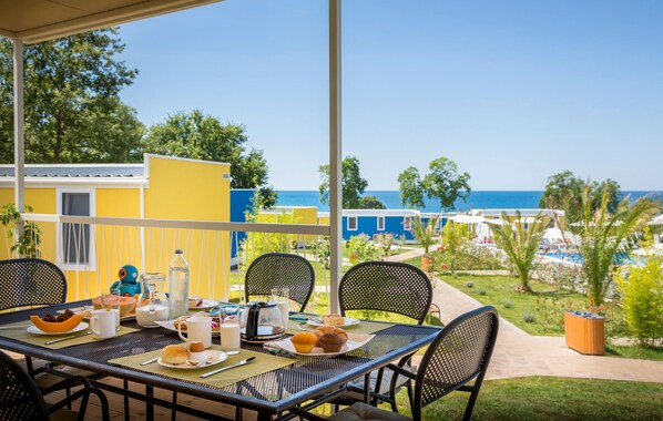Une table dressée pour le petit-déjeuner, avec vue sur la mer et des bâtiments colorés en arrière-plan.