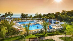 Zona de piscina amb gandules i ombrelles, envoltada de vegetació i vistes al mar.