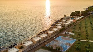 Una zona costera amb una filera de cases davant de la platja, una pista de bàsquet i vistes al mar durant el capvespre.