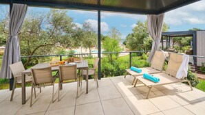 Ein überdachter Essbereich im Freien mit Tisch für zwei Personen, Stühlen und Blick auf Pool und Grünfläche.