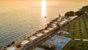 Eine Küstenlandschaft mit einer Reihung von Strandbungalows, einem Basketballplatz und Blick auf das Meer bei Sonnenuntergang.