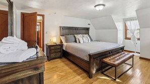 A bedroom with a wooden bed, a bedside table with a lamp, a bench, and a large mirror. - Church Street Retreat - Downtown Location! (Wisconsin Dells)