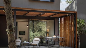 An outdoor seating area with a table and chairs, a hanging light fixture, and a view of trees through a glass wall. - Lovely home in Njivice with swimming pool (Njivice)