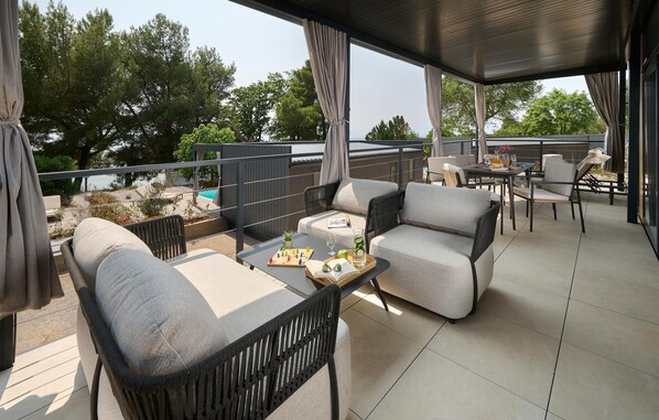 A covered outdoor seating area with cushioned chairs and a table, overlooking a pool and greenery. - Awesome home in Njivice with WiFi (Njivice)