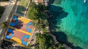 An aerial view of a coastal area with a basketball court, a wooden deck, and clear turquoise waters. - Gorgeous home in Njivice with WiFi (Njivice)