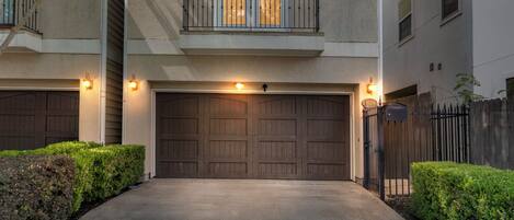 A residential building with a double garage door, a balcony with a railing, and a gated driveway.