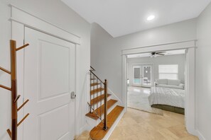 Ein Flur, der in ein Schlafzimmer mit Bett, Deckenventilator und Balkonblick führt.