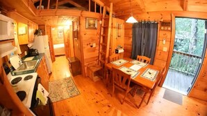 A wooden cabin interior with a kitchen, dining area, and a large window.