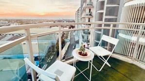 Un edificio de gran altura con balcón de vidrio, mobiliario exterior blanco y vista panorámica de la ciudad.