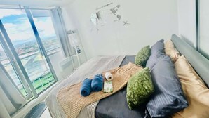 Una habitación de hotel moderna con un ventanal grande, una cama con manta a rayas y un adhesivo de aviones en la pared.