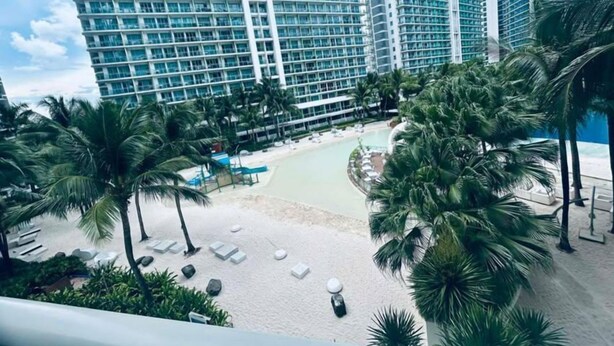 Un hotel moderno con piscina, palmeras y sillas de playa.