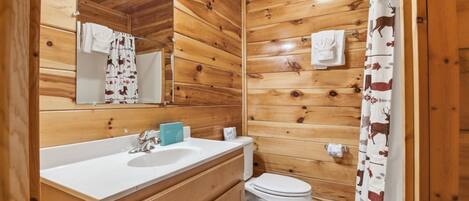 Une salle de bain aux murs lambrés, équipée d’un lavabo, d’un miroir et de toilettes.