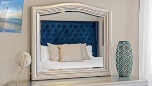 Una cama con cabecera capitonada, un florero decorativo y un globo terráqueo sobre un tocador.
