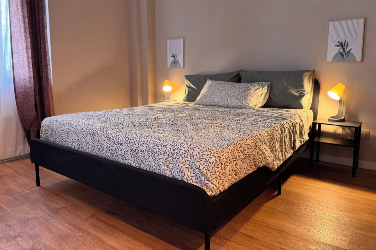 A neatly made bed with a patterned bedspread, two bedside lamps, and a framed picture on the wall.