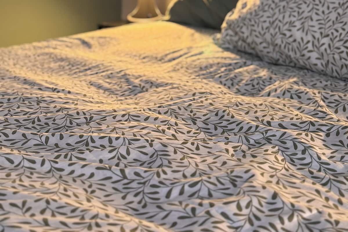 A bed with a patterned bedspread, a bedside lamp, and a framed artwork on the wall.