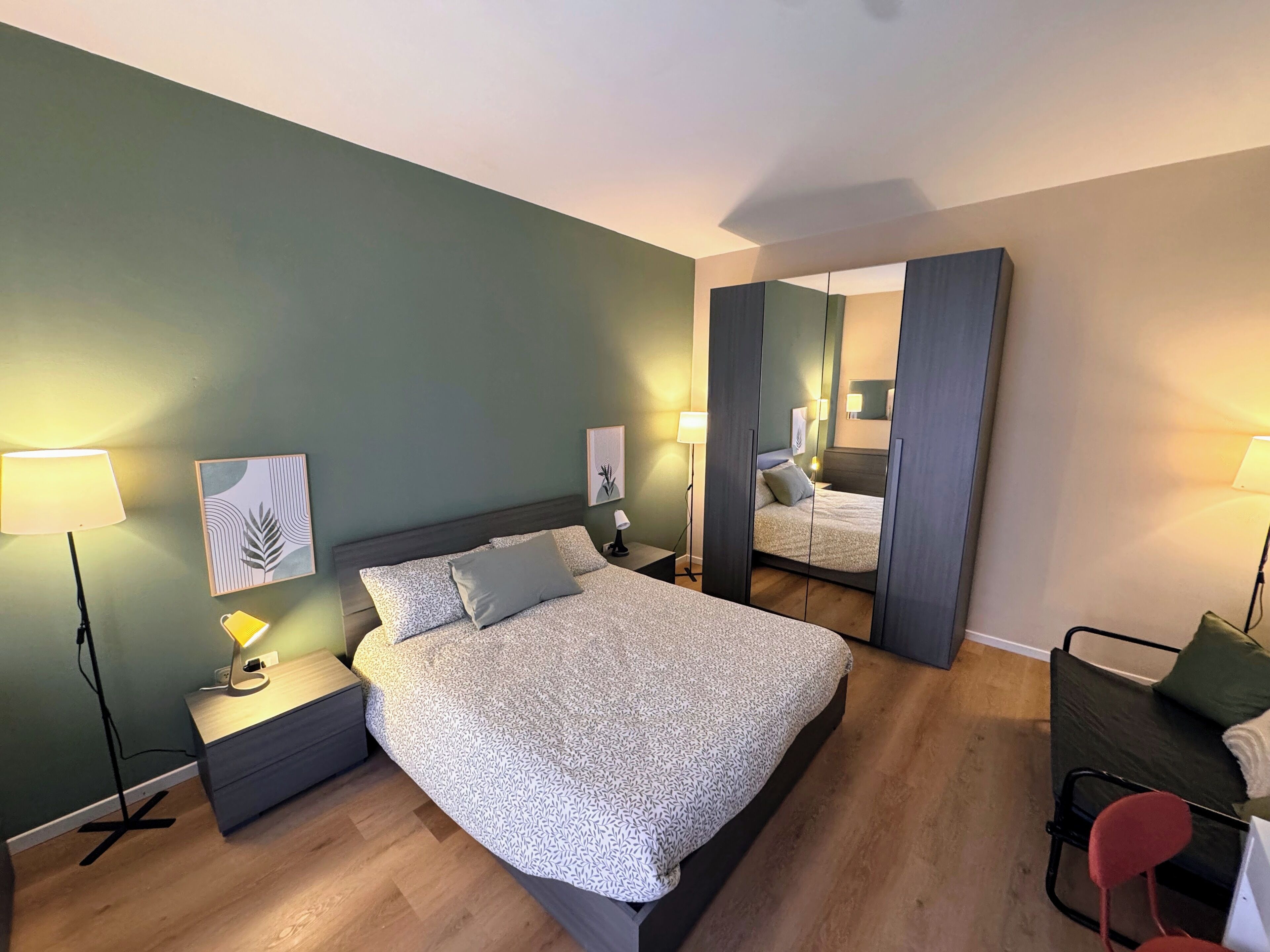 Ein modernes Schlafzimmer mit einem großen Bett, Nachttischlampen, einem Schreibtisch und einem Spiegel.