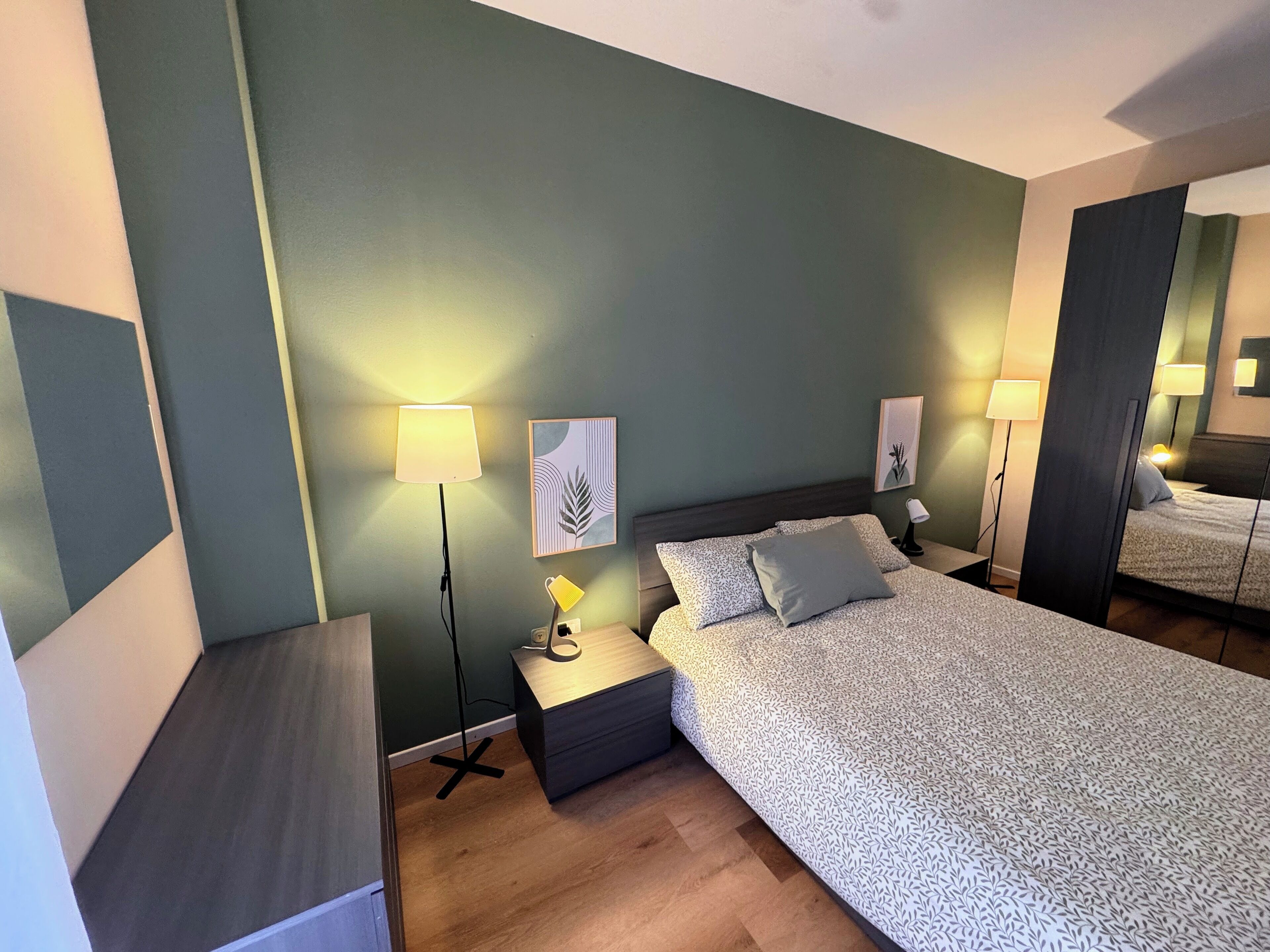 Un dormitorio moderno con una cama grande, dos mesitas de noche, una lámpara de pie y un espejo.