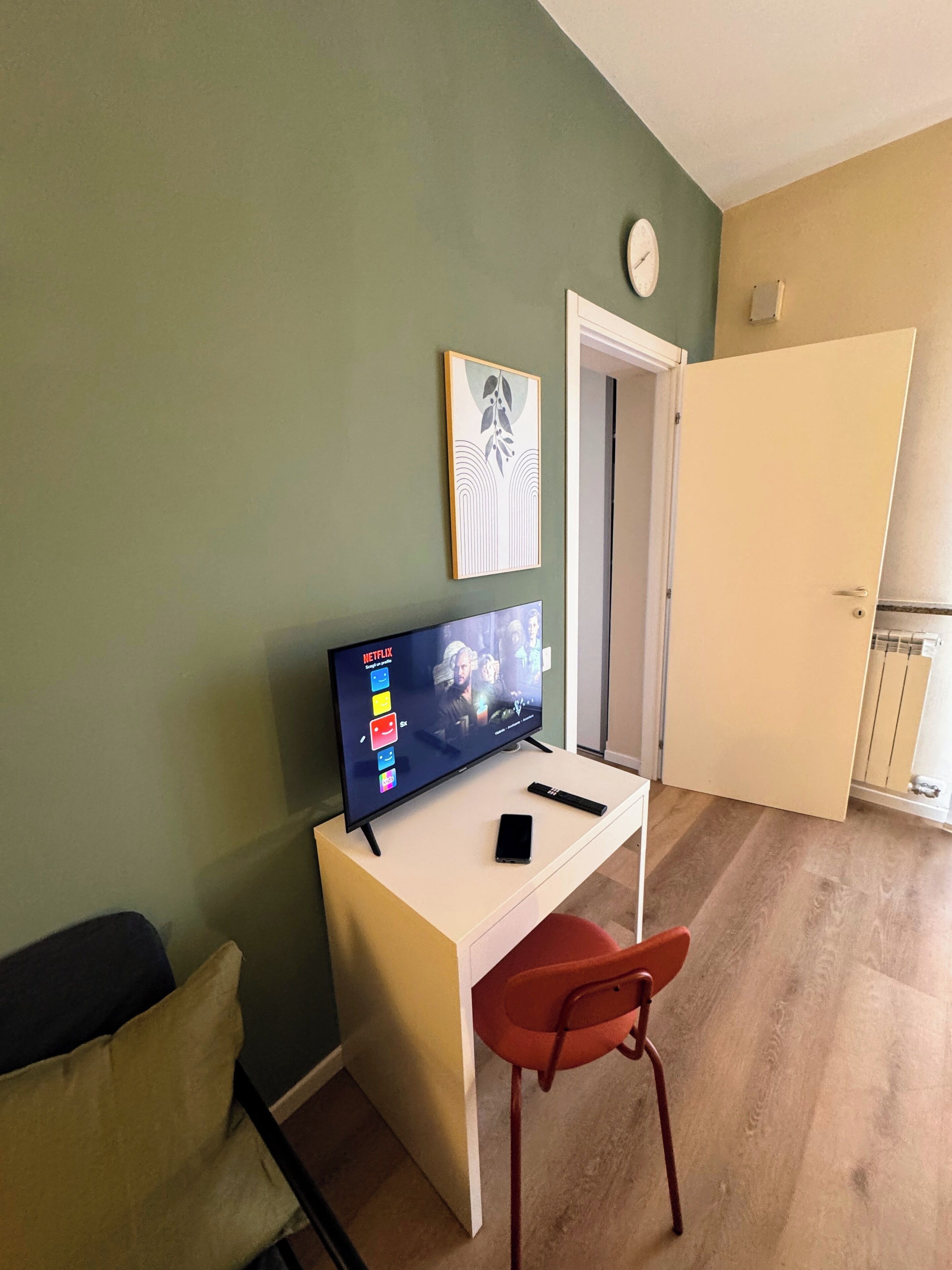A room with a white desk, a television displaying a Netflix interface, a smartphone, and a red chair.