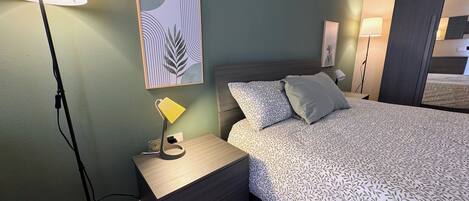Ett välordnat sovrum med en säng, sängbord, en lampa och ett konstverk som hänger på väggen.