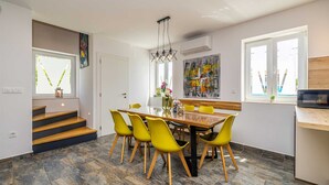 A modern dining area with a wooden table and yellow chairs, a staircase, and a large abstract painting on the wall. - Holiday house MARLY with private pool (Kras)