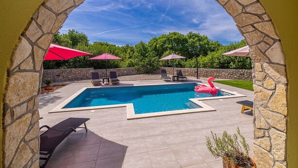 A swimming pool with a stone archway, lounge chairs, and umbrellas. - Holiday house MARLY with private pool (Kras)