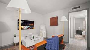A modern living room with a white sofa, a coffee table, and a TV displaying a show. There is a lamp, a mirror, and a door leading to another room. - Austin Escape • Pool • 5 mins to Hyde Park UT (Austin)