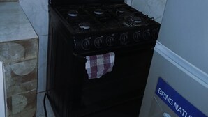 Una cocina pequeña con estufa negra, azulejos de mármol blanco y refrigerador azul.