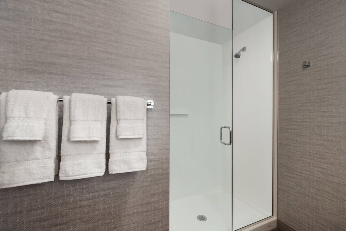 A modern bathroom with a glass shower enclosure, a towel rack with three towels, and a textured wall.