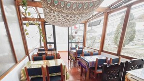 A restaurant with wooden tables and chairs, large windows, and a decorative ceiling. - Hotel El Geranio (Quito)