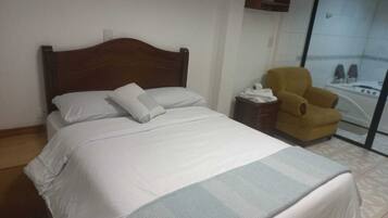 Una habitación de hotel con una cama, una silla y un baño visible a través de una puerta de vidrio.