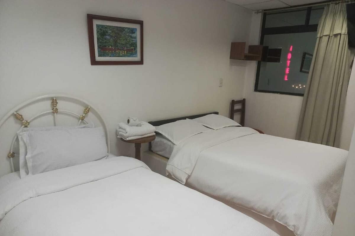 A hotel room with two beds, a small table with a telephone, and a painting on the wall.